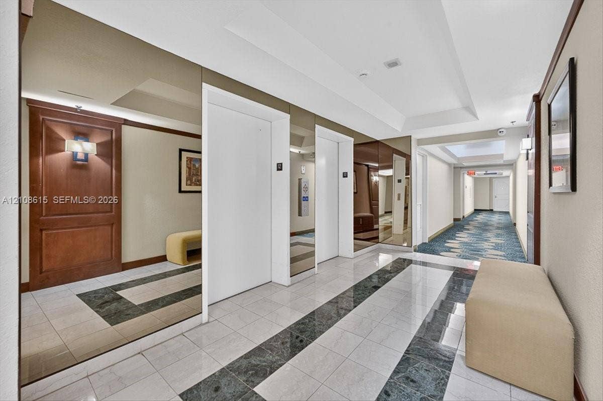 9455 Collins Avenue, #1201, Surfside, FL 33154 Elevator lobby featuring floor-to-ceiling wall mirrors, polished stone tile flooring with decorative inlay, and wood-paneled accents