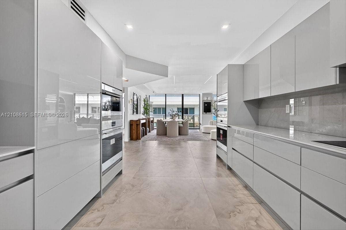 9455 Collins Avenue, #1201, Surfside, FL 33154 Contemporary kitchen featuring high-gloss cabinetry, large-format tile flooring, stone-surfaced countertops, and built-in stainless steel double ovens