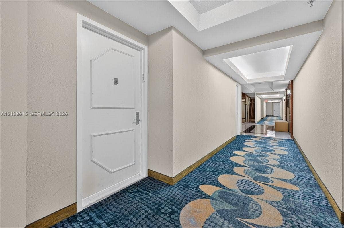 9455 Collins Avenue, #1201, Surfside, FL 33154 Interior corridor featuring a white paneled door with metal hardware, recessed ceiling lighting, and patterned carpeting