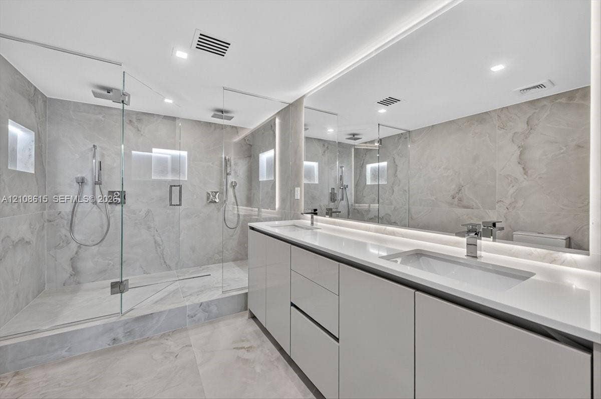 9455 Collins Avenue, #1201, Surfside, FL 33154 Bathroom featuring a walk-in shower with glass enclosure, large-format tile surround, dual vanity with undermount sinks, full-width mirror, and integrated lighting