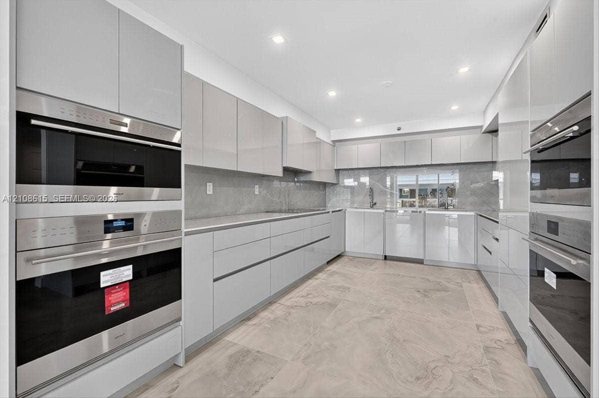 9455 Collins Avenue, #1201, Surfside, FL 33154 Modern kitchen featuring high-gloss cabinetry, stone-finish tile flooring, integrated stainless steel ovens, and recessed lighting