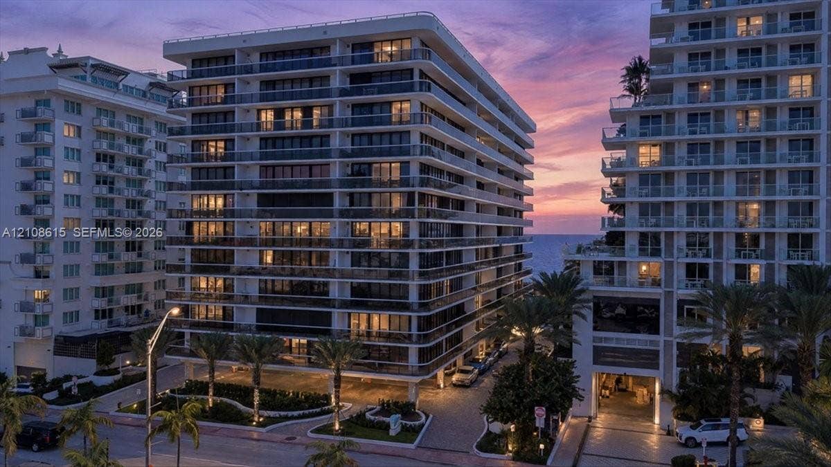9455 Collins Avenue, #1201, Surfside, FL 33154 High-rise building exterior featuring glass-railed balconies, a paved porte-cochre entry, ground-level landscaping, and palm trees