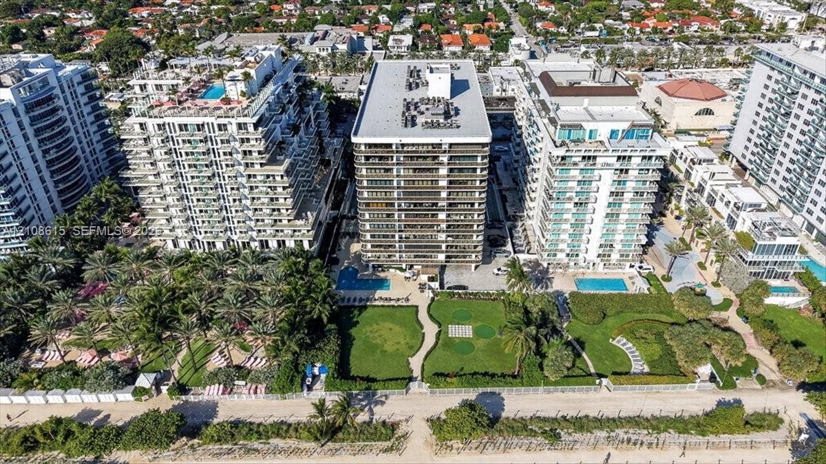 9455 Collins Avenue, #1201, Surfside, FL 33154 Aerial perspective of a high-rise residential building featuring an outdoor swimming pool, expansive landscaped lawn, mature palm trees, and direct beach access