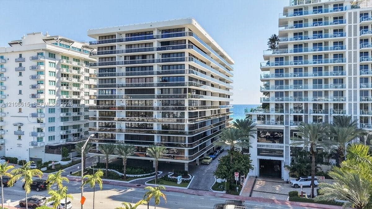 9455 Collins Avenue, #1201, Surfside, FL 33154 Multi-story residential building featuring floor-to-ceiling glass windows, wraparound balconies with railings, and palm-lined grounds