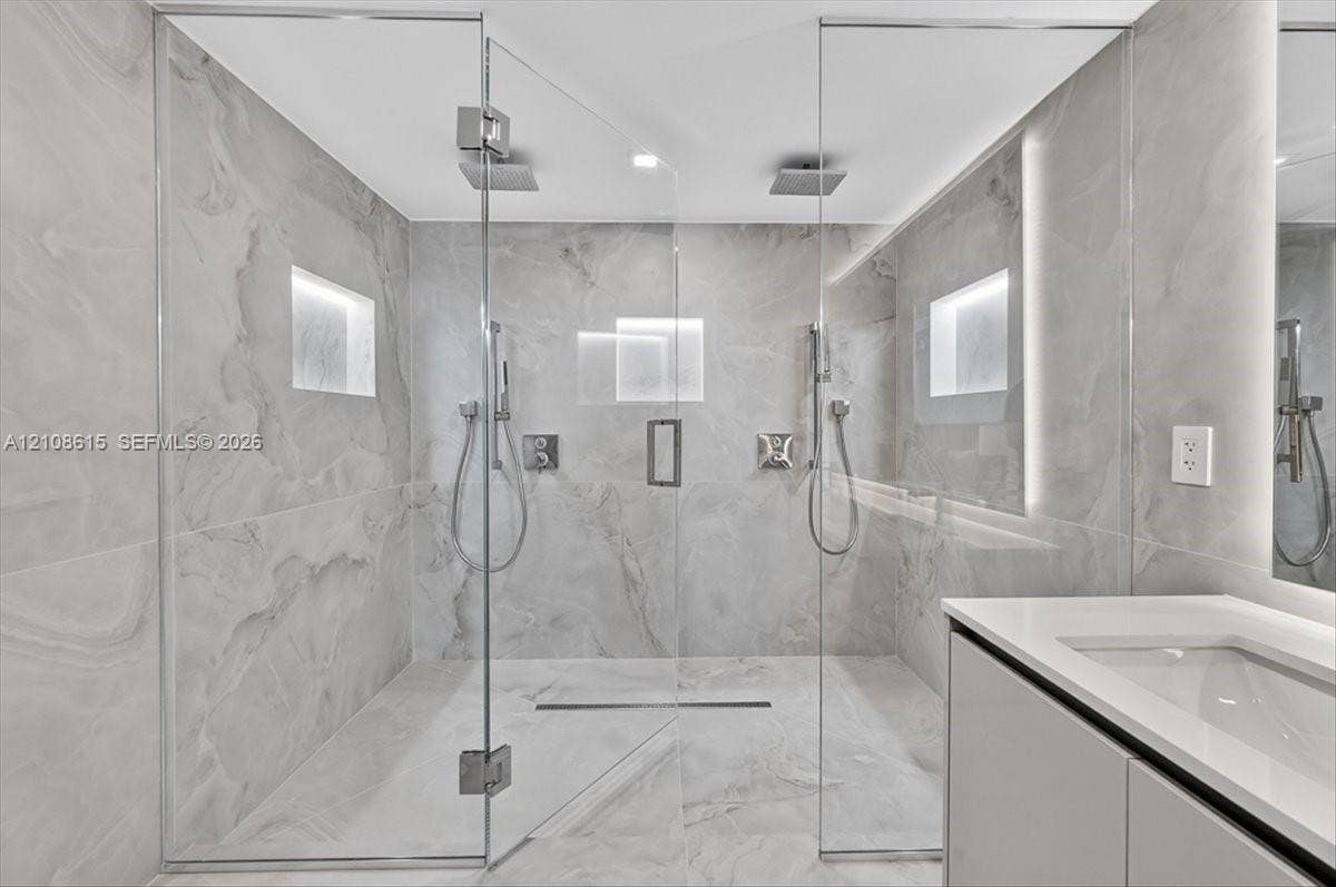 9455 Collins Avenue, #1201, Surfside, FL 33154 Walk-in shower featuring floor-to-ceiling stone-finish tile, dual ceiling-mounted rainfall showerheads, handheld sprayers, recessed wall niches, and frameless glass enclosure