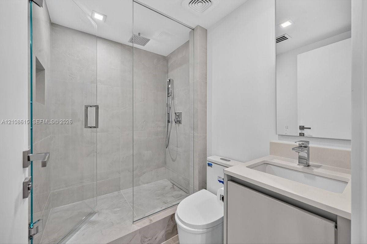 9455 Collins Avenue, #1201, Surfside, FL 33154 Bathroom featuring a glass-enclosed shower with a rainfall showerhead, large-format tile surround, integrated shower niche, wall-mounted vanity with a rectangular sink, and polished chrome fixtures