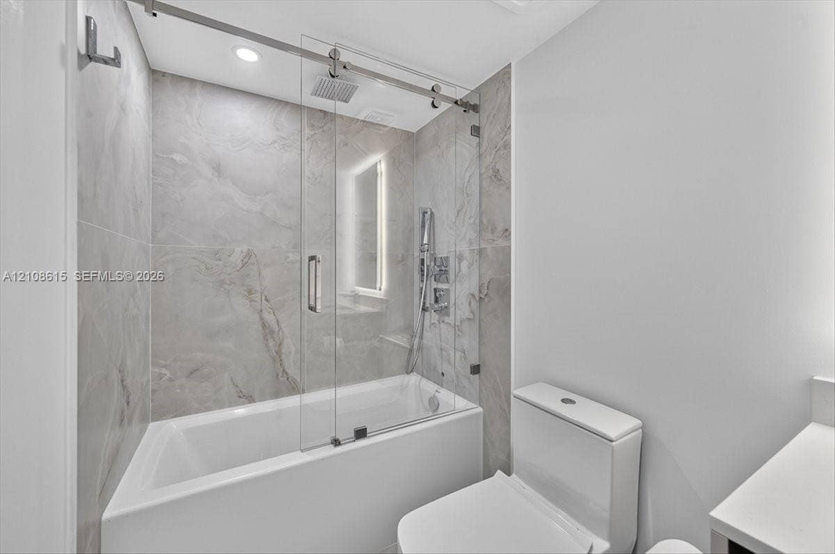 9455 Collins Avenue, #1201, Surfside, FL 33154 Shower with glass sliding enclosure, floor-to-ceiling stone-finish tile surround, ceiling-mounted rainfall showerhead, and integrated handheld fixture