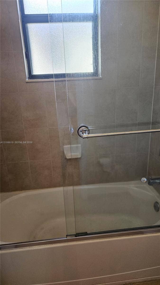 Bathtub with a glass sliding enclosure, integrated soap dish, and neutral wall tile surround