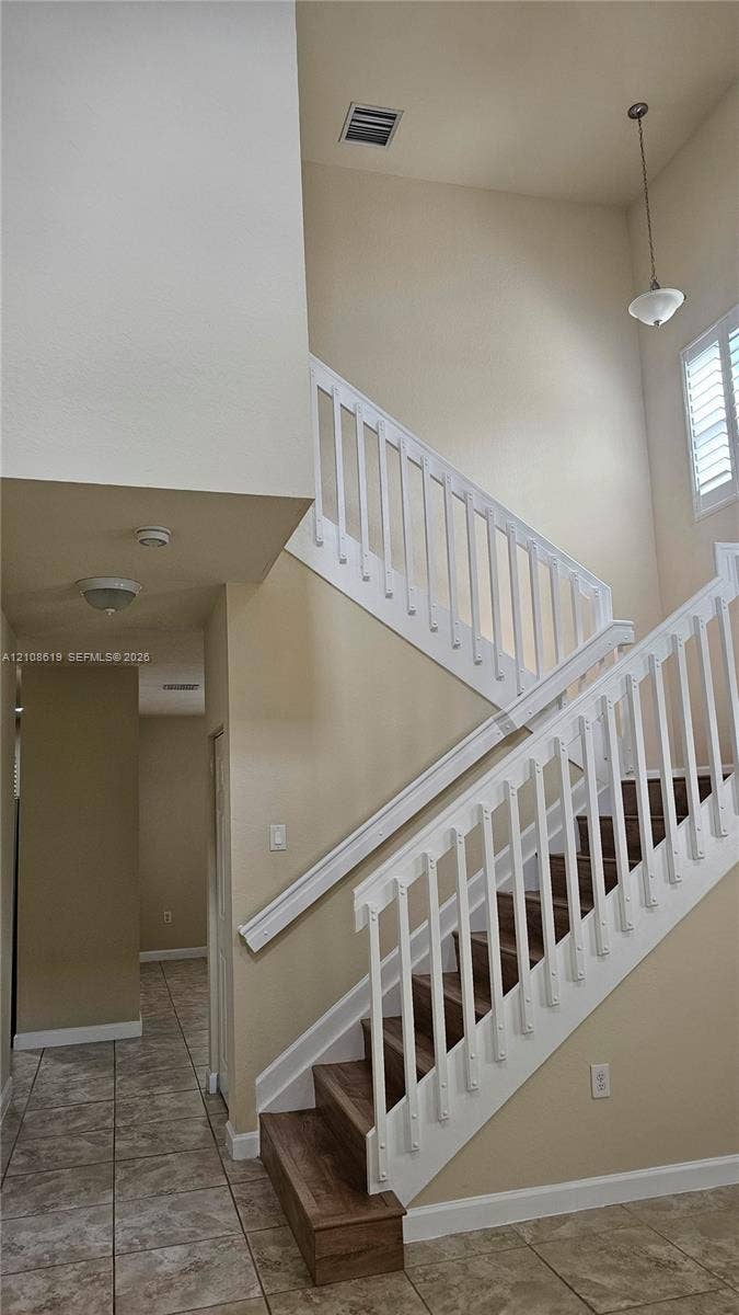 Staircase featuring wood-finish treads, white balusters, high ceilings, tile flooring, and a pendant light fixture