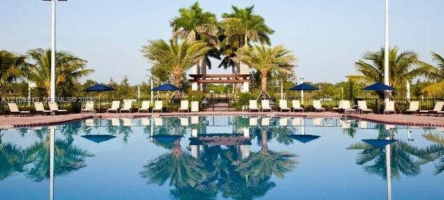 Swimming pool with surrounding paver deck, wooden pergola, and mature palm trees