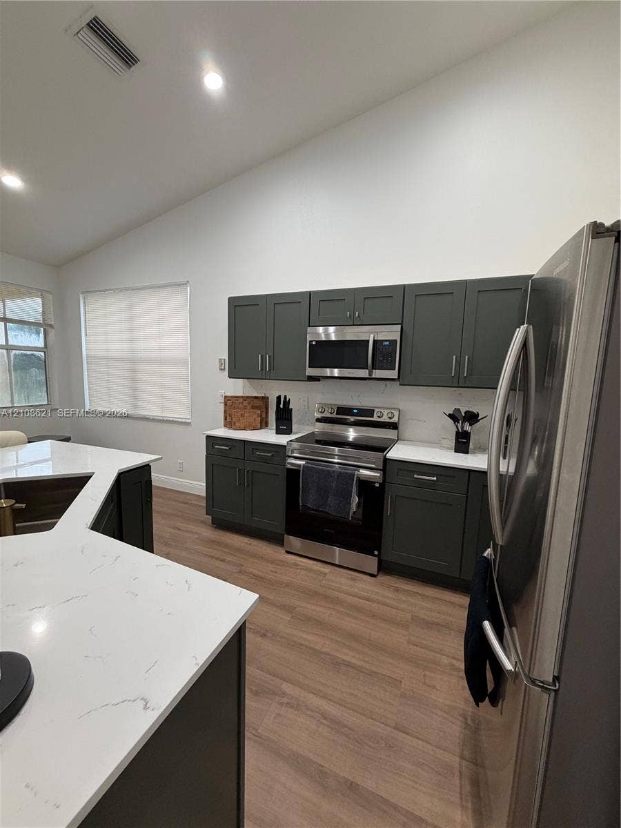 Kitchen featuring dark cabinetry, quartz countertops, stainless steel appliances, a multi-angled island, and wood-finish flooring
