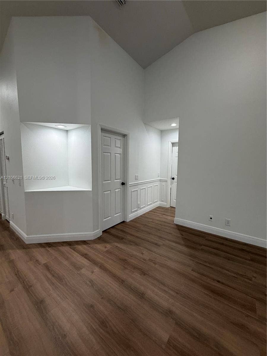 Vaulted ceilings, wood-finish flooring, recessed architectural niche with integrated lighting, and wainscoting detailing