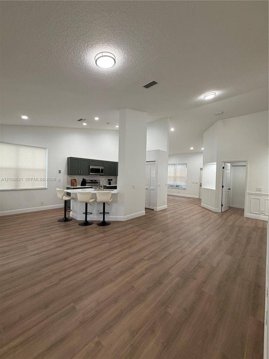 Open-concept interior featuring wood-finish flooring, dark cabinetry, recessed lighting, and a breakfast bar with stone-surface countertop