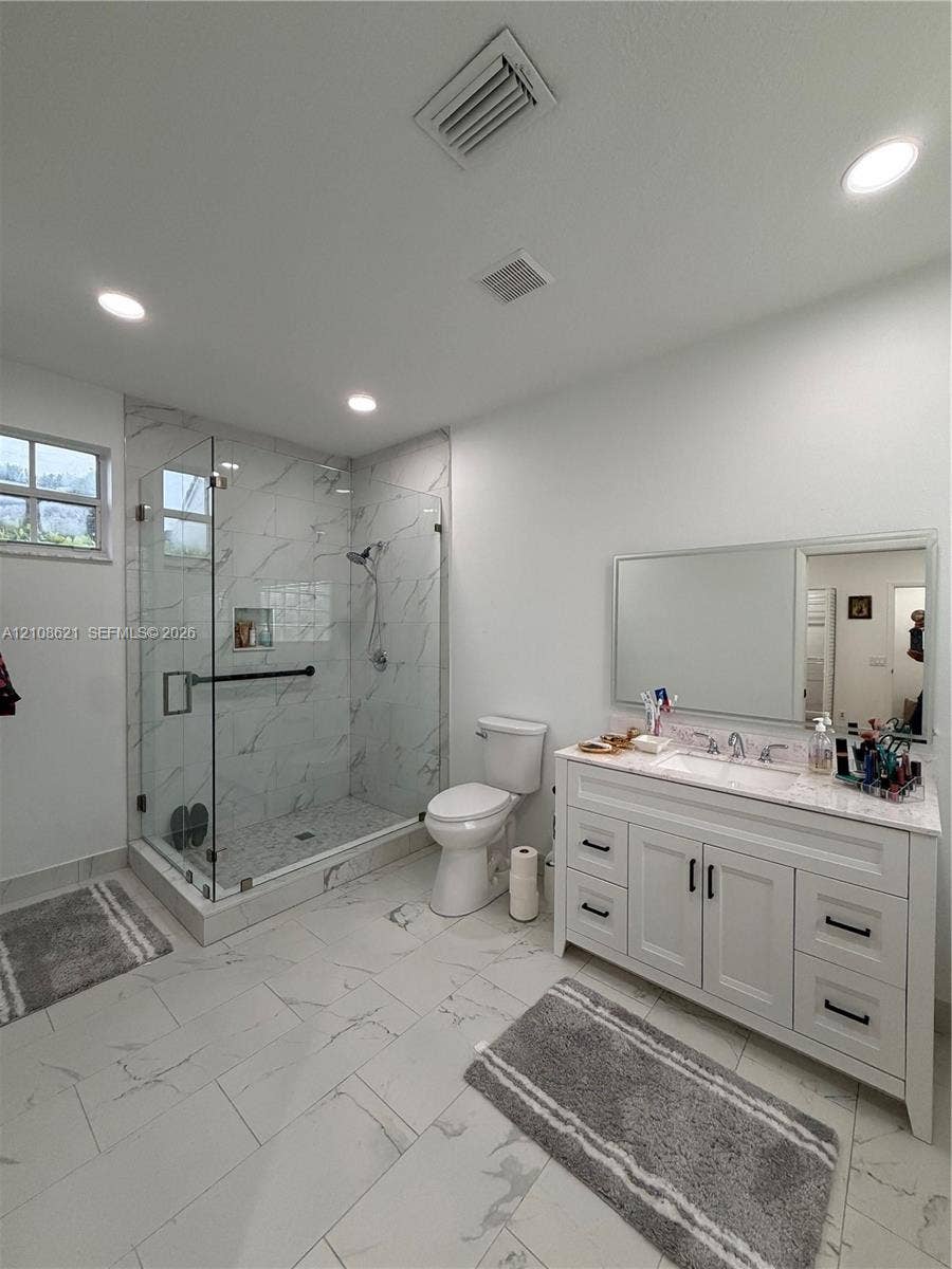 Bathroom featuring a glass-enclosed walk-in shower with tile surround, white vanity with stone countertop, recessed lighting, and large-format tile flooring