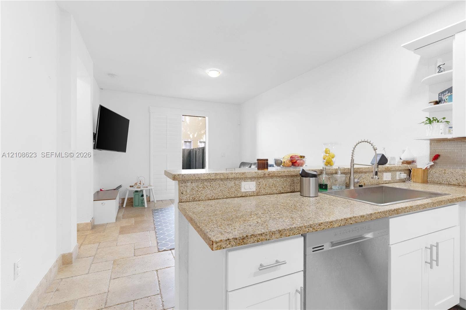 Kitchen featuring stone-finish countertops, stainless steel undermount sink with a gooseneck faucet, white shaker-style cabinetry, built-in dishwasher, and stone-tile flooring