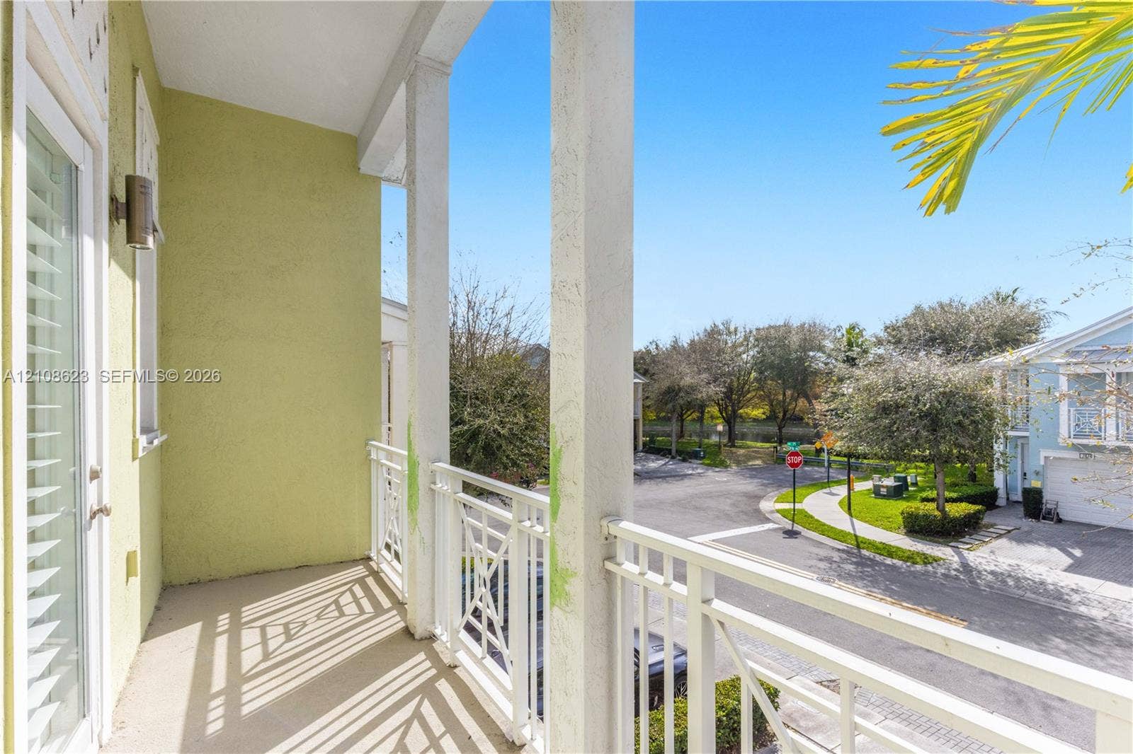 Covered balcony featuring white metal railings, structural support columns, and an exterior wall-mounted light fixture