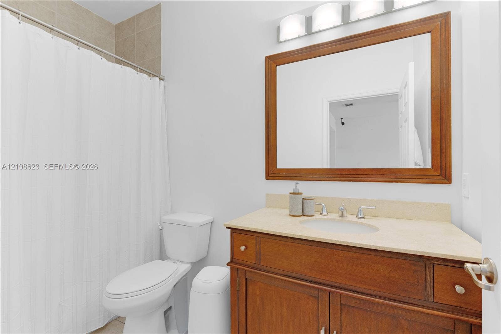 Bathroom featuring a wood-finish vanity with a neutral solid-surface countertop, an oval under-mount sink, a framed wall mirror, and a three-bulb vanity light fixture