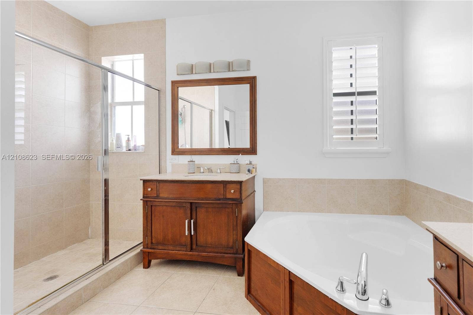 Bathroom featuring a wood-finish vanity with a stone countertop, corner soaking tub with wood-finish surround, walk-in glass-enclosed shower, tiled flooring, and framed wall mirror