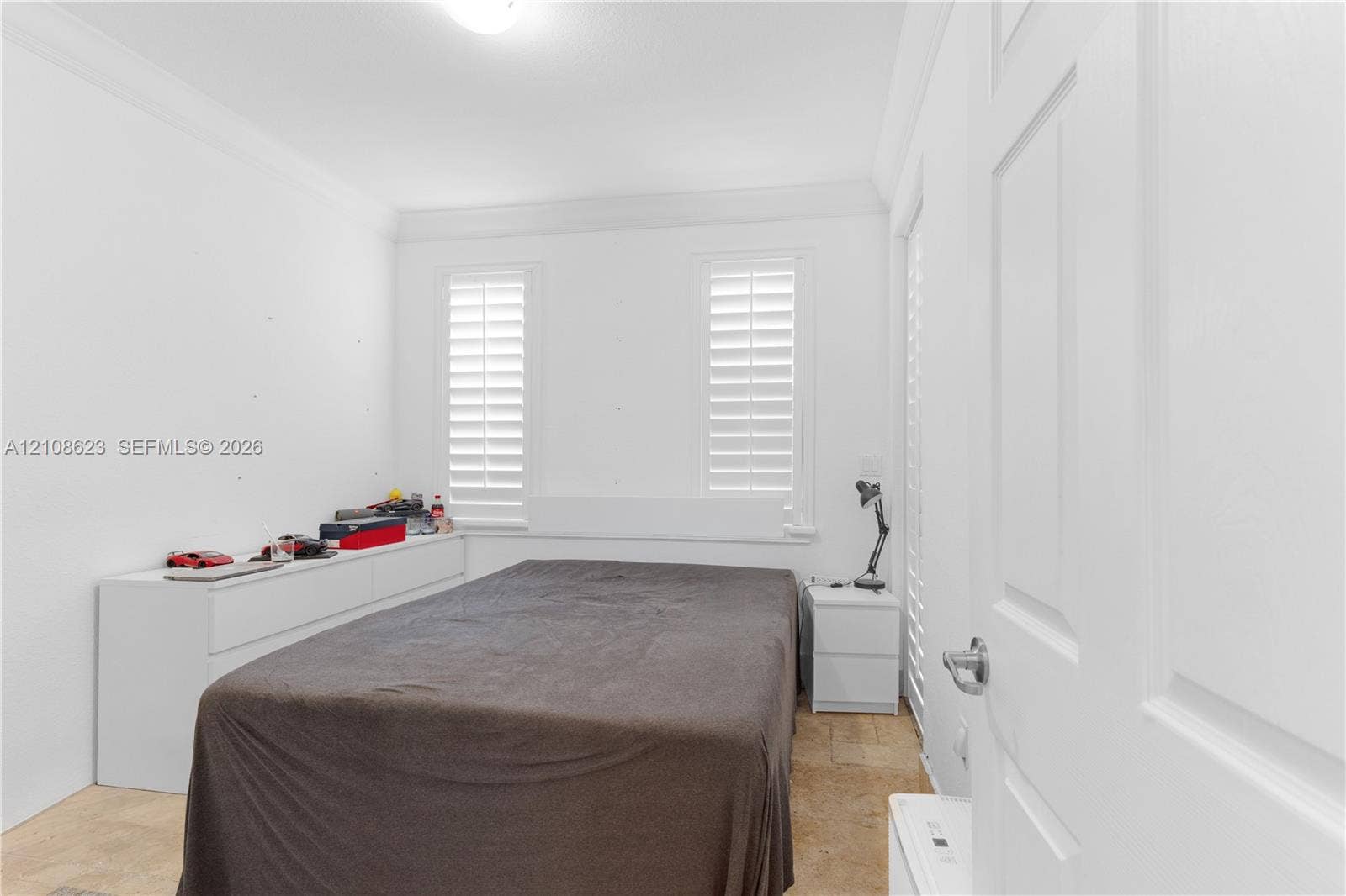 Room featuring white plantation shutters, crown molding, and stone-finish flooring