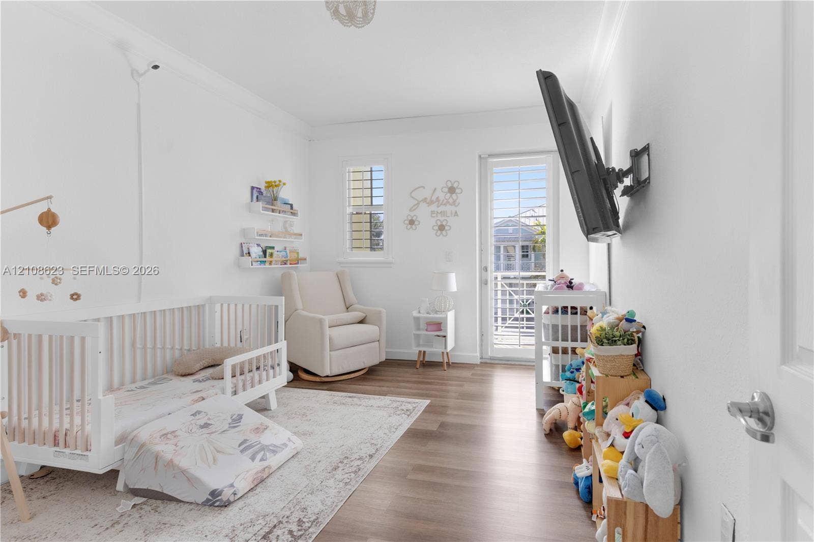 Room featuring wood-finish flooring, crown molding, built-in shelving, and a glass-paned door