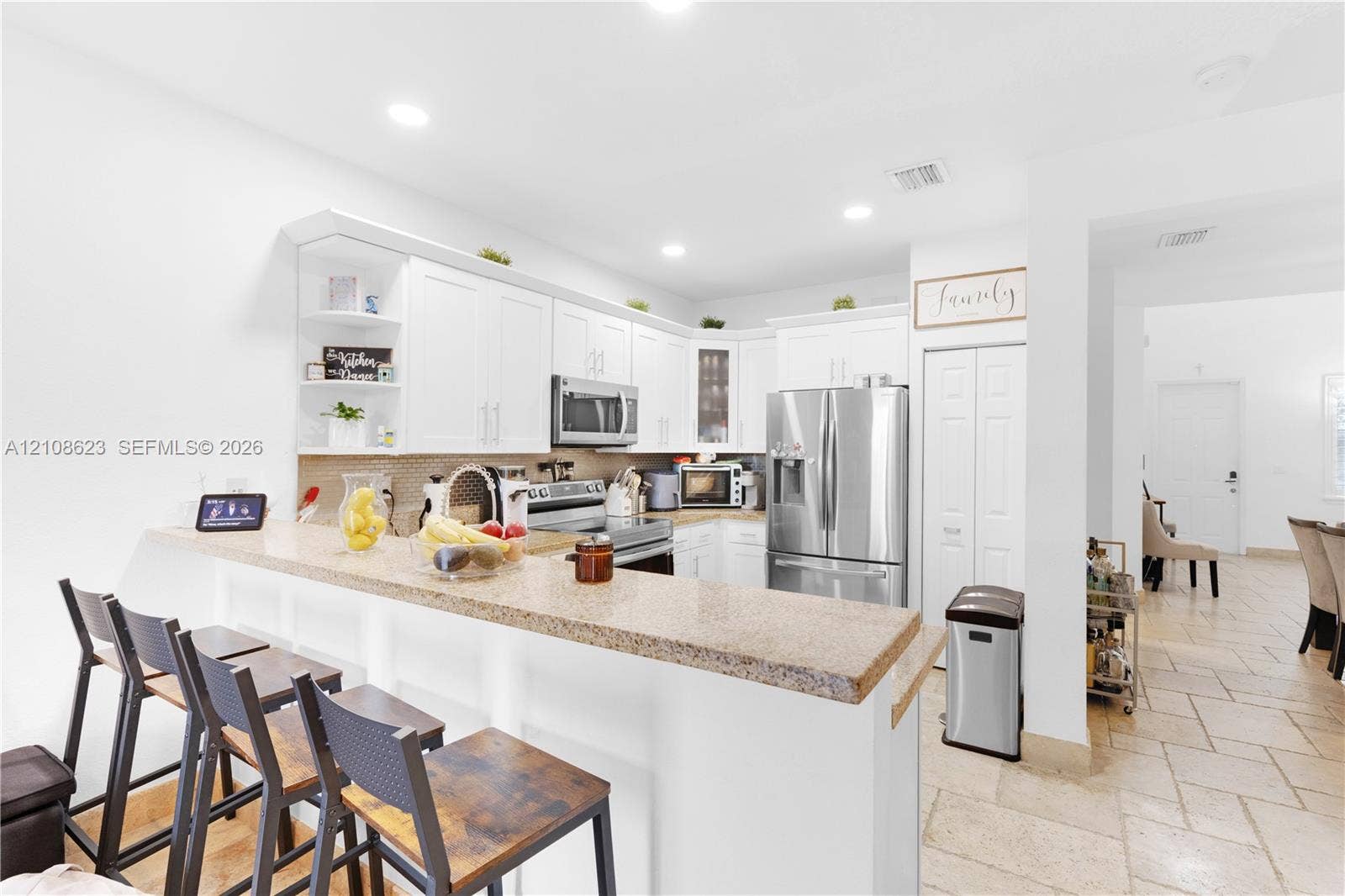 Kitchen featuring white cabinetry, stone-finish countertops, stainless steel appliances, a breakfast bar, and tile flooring