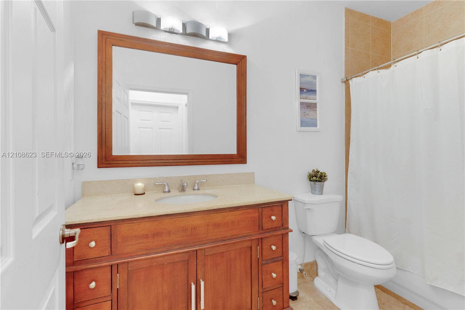 Bathroom featuring a wood-finish vanity with a neutral countertop, undermount sink, multi-light fixture, and framed wall mirror