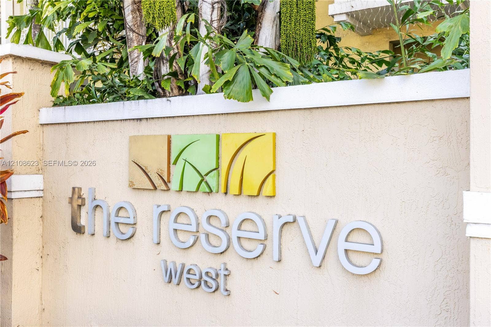 Stucco-finished masonry signage featuring dimensional lettering and sculptural metal detailing, complemented by mature tropical landscaping