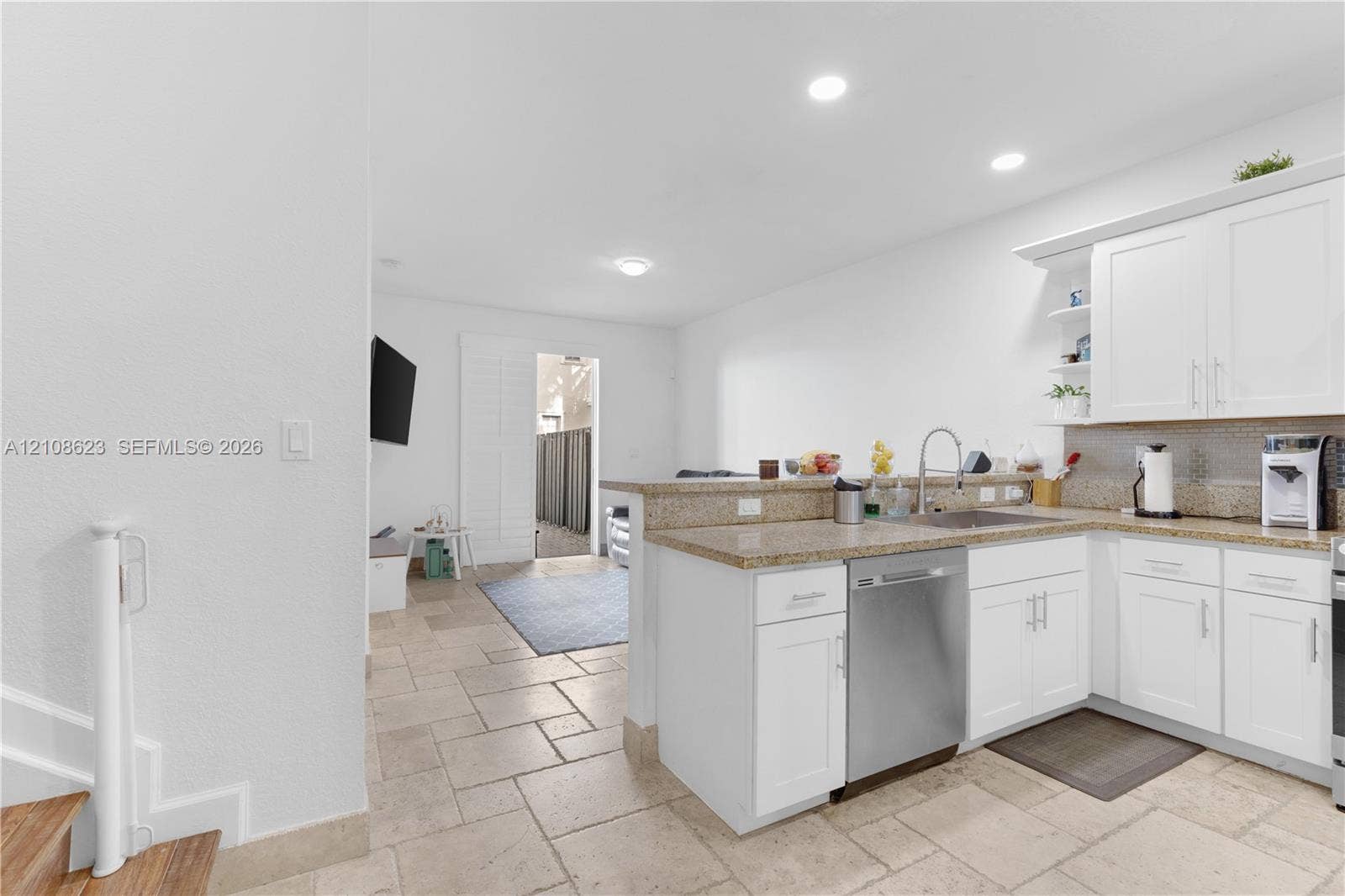 Kitchen featuring white shaker-style cabinetry, stone-finish countertops, stainless steel dishwasher, undermount sink, and stone-tile flooring