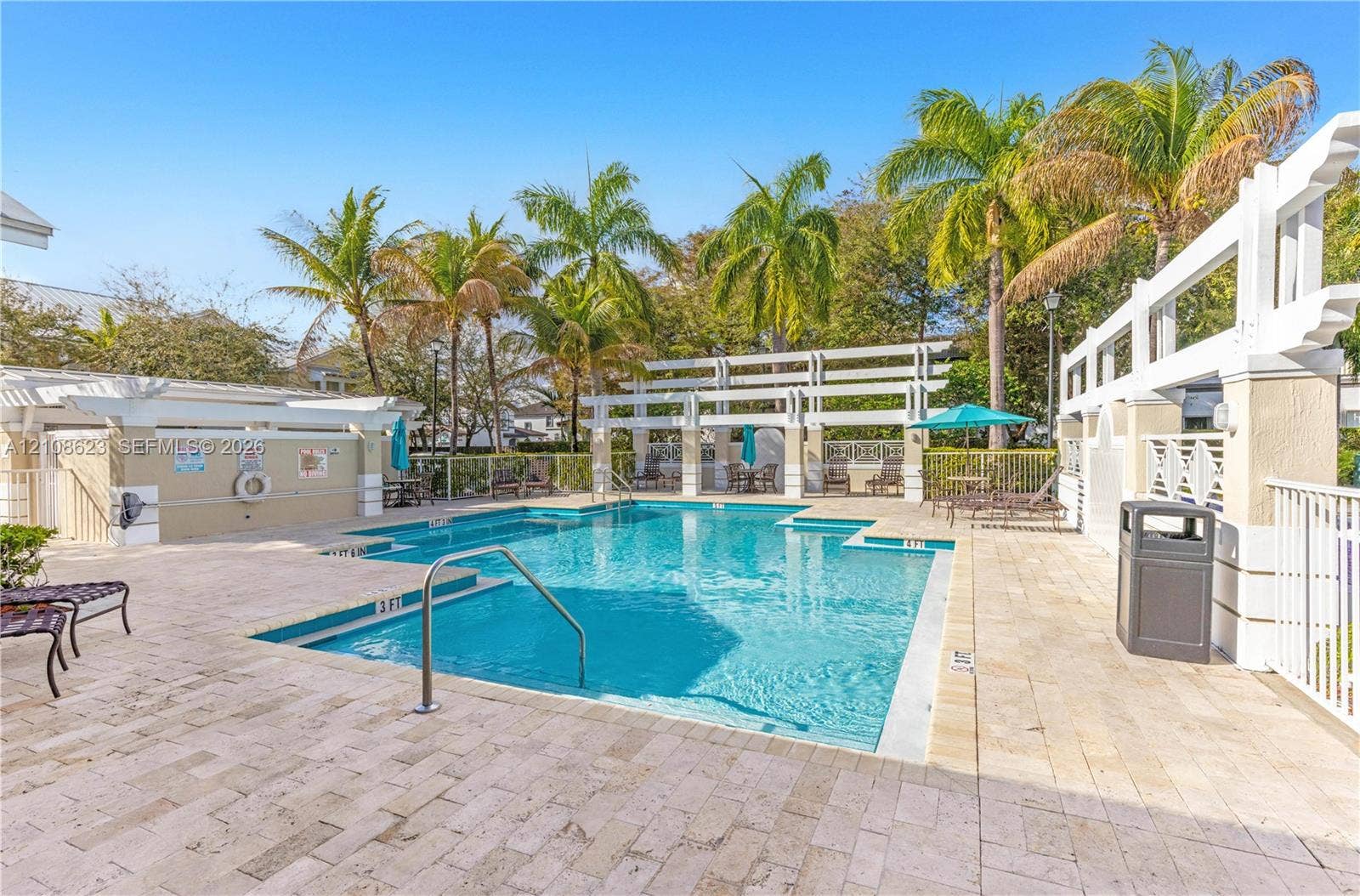 Swimming pool with paved surround, white trellis structures, and mature palm trees