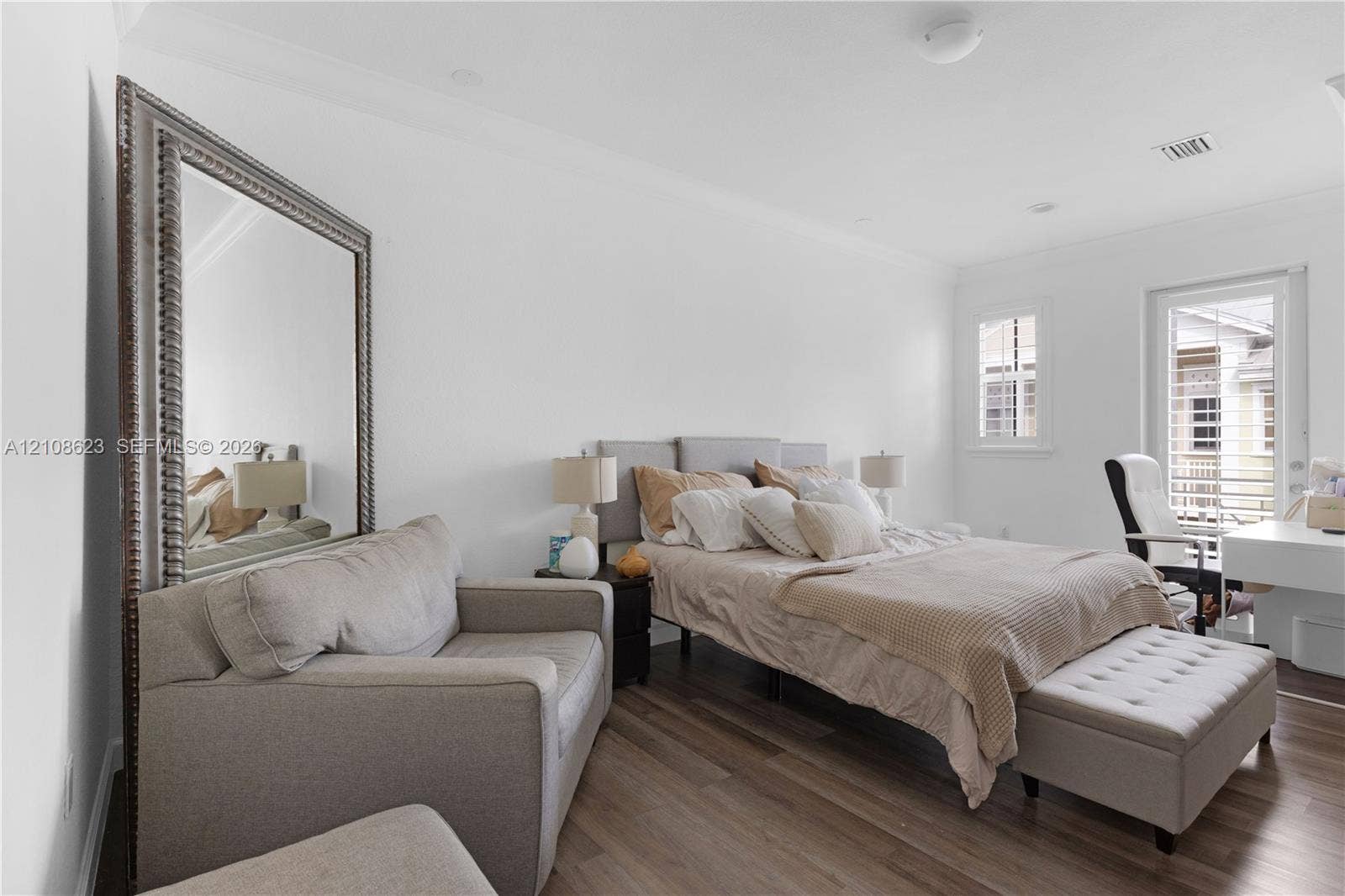Neutral-toned room featuring wood-finish flooring, crown molding, and a full-length wall mirror with a metallic frame