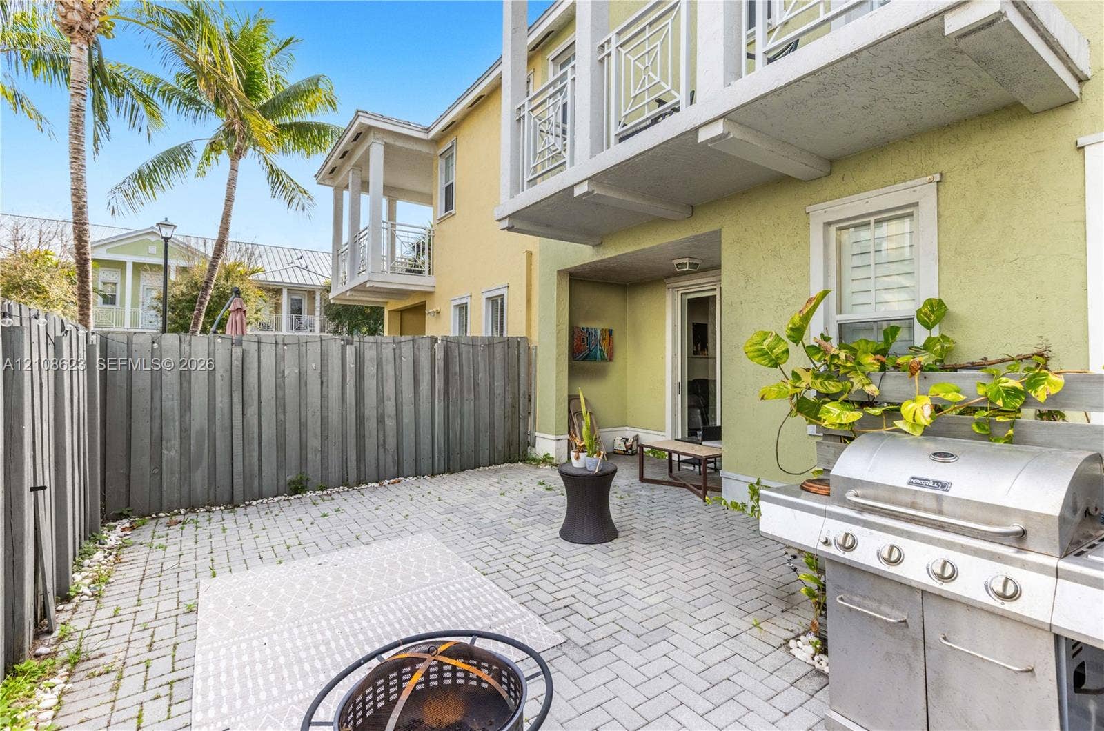 Private courtyard featuring herringbone-patterned stone pavers, privacy fencing, and two elevated balconies with geometric metal railings