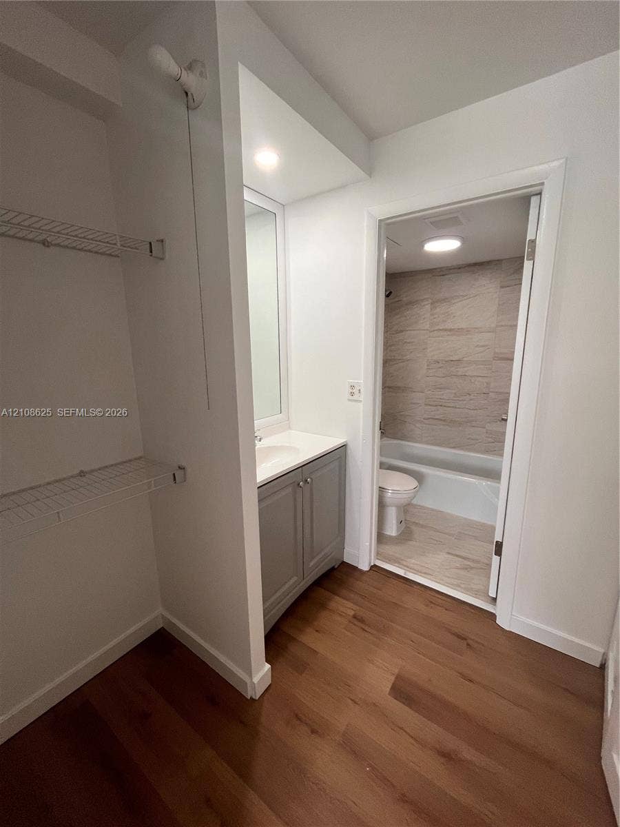 3650 Inverrary Drive, #1Q, Lauderhill, FL 33319 Bathroom featuring wood-finish flooring, a grey vanity with a solid-surface countertop, an inset sink, and a tiled shower-tub combination