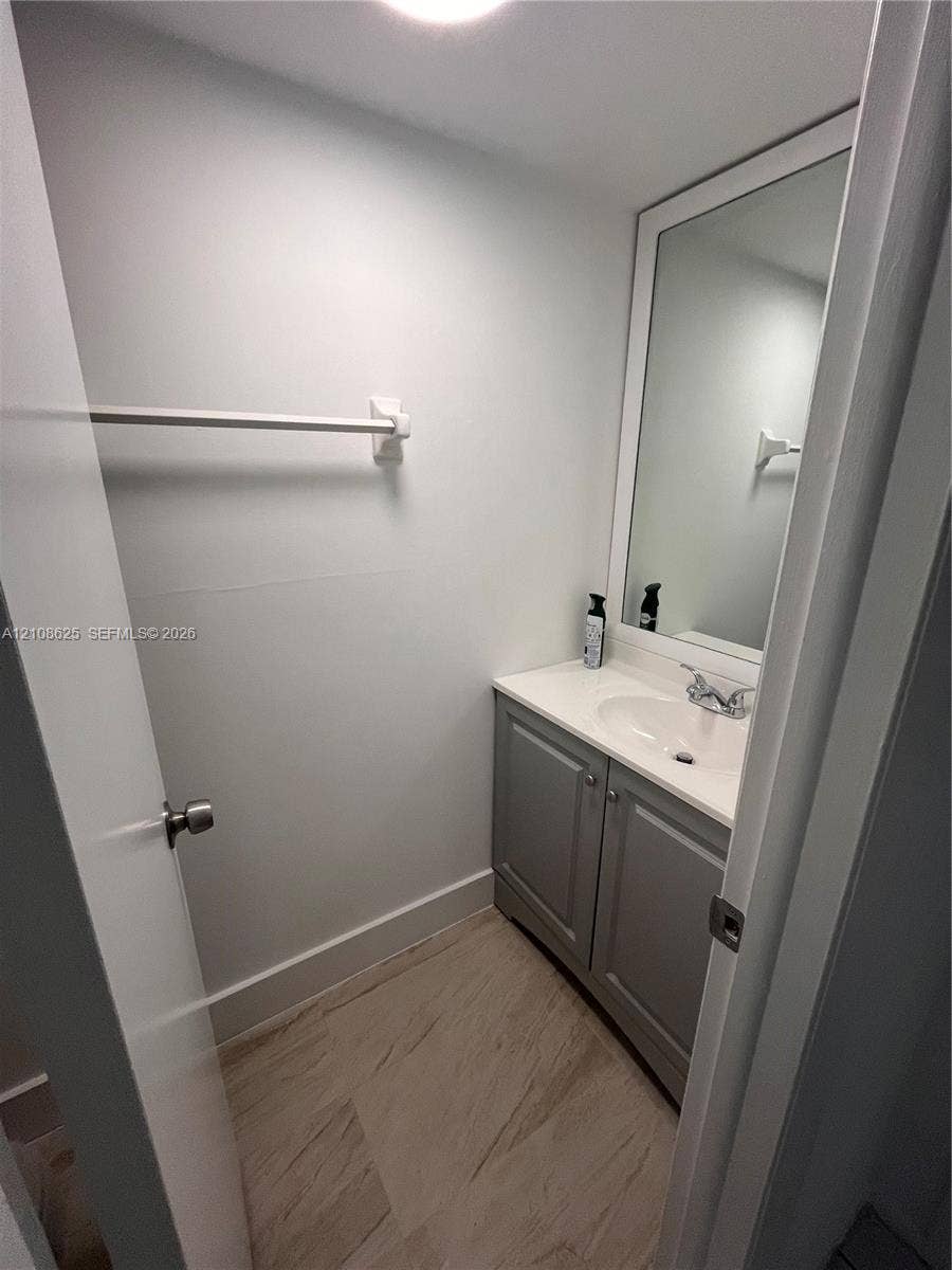 3650 Inverrary Drive, #1Q, Lauderhill, FL 33319 Bathroom featuring a vanity with grey cabinetry, a solid-surface countertop with an integrated basin, a wall-mounted mirror with a white frame, and wood-finish flooring