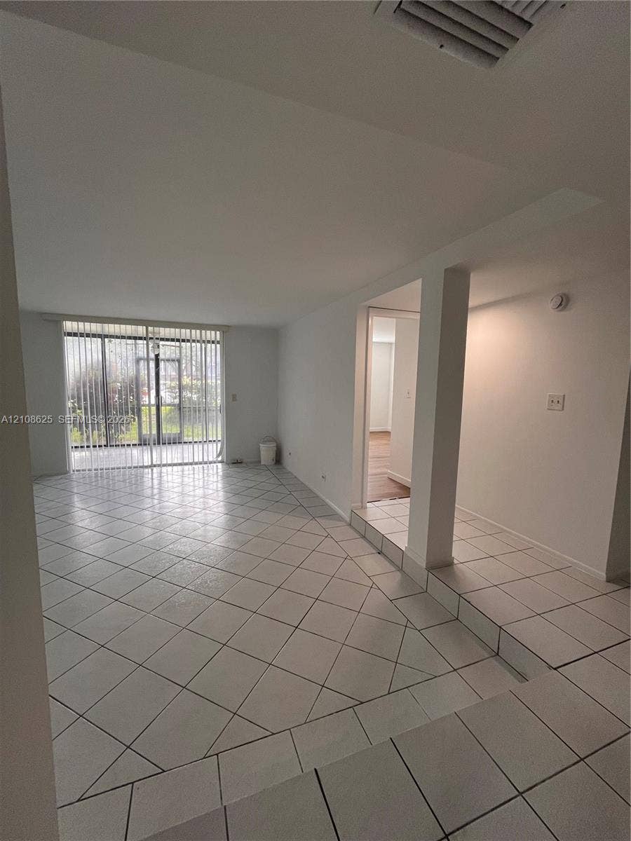 3650 Inverrary Drive, #1Q, Lauderhill, FL 33319 Open-concept interior featuring large-format ceramic tile flooring laid on the diagonal, architectural support column, and full-height sliding glass doors with vertical blinds