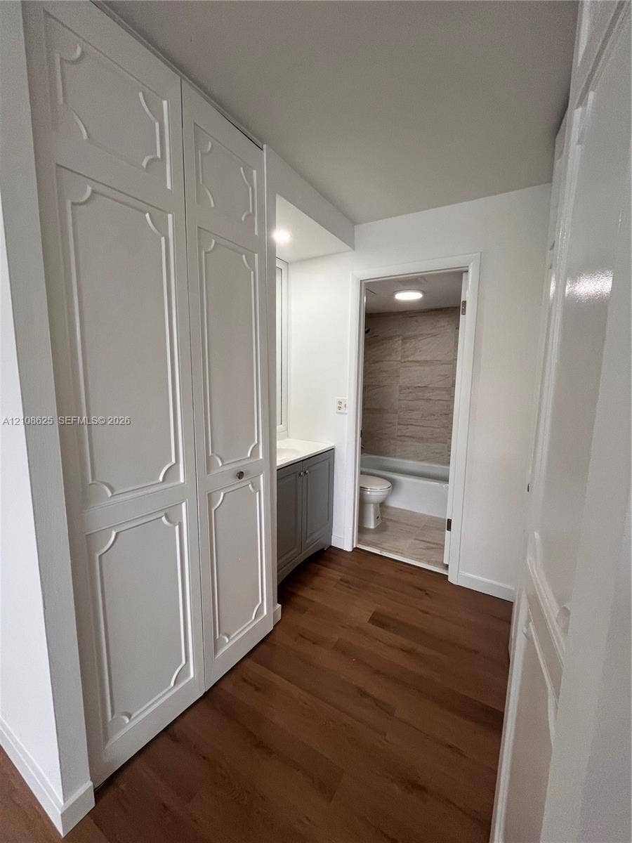 3650 Inverrary Drive, #1Q, Lauderhill, FL 33319 Wood-finish flooring, full-height cabinetry with decorative paneling, stone-topped vanity, and tile-surround bathtub