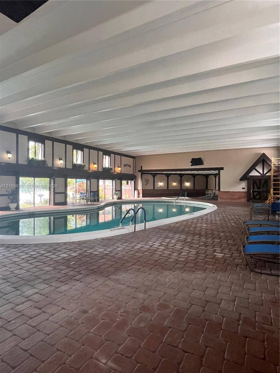 3650 Inverrary Drive, #1Q, Lauderhill, FL 33319 Indoor pool area featuring a brick paver floor, exposed beam ceiling, sliding glass doors, and half-timbered architectural detailing