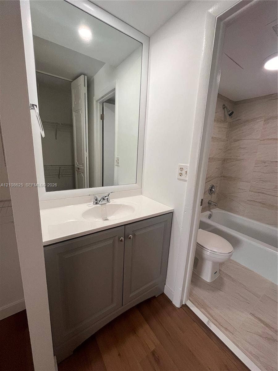 3650 Inverrary Drive, #1Q, Lauderhill, FL 33319 Bathroom featuring a grey vanity cabinet with a white countertop, large framed wall mirror, and a tile-surround bathtub