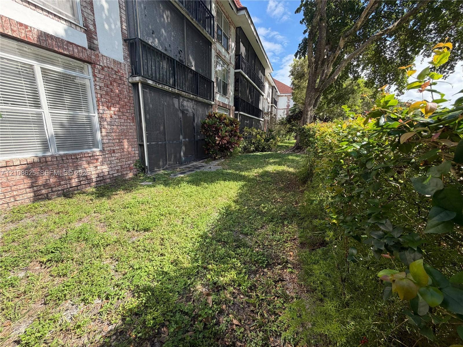 3650 Inverrary Drive, #1Q, Lauderhill, FL 33319 Exterior facade featuring red brick masonry, multi-level screened balconies, and surrounding mature landscaping