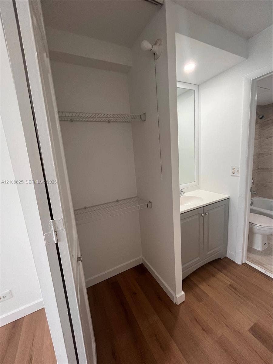 3650 Inverrary Drive, #1Q, Lauderhill, FL 33319 Closet featuring white wire shelving, wood-finish flooring, and a vanity with a white countertop and gray cabinetry