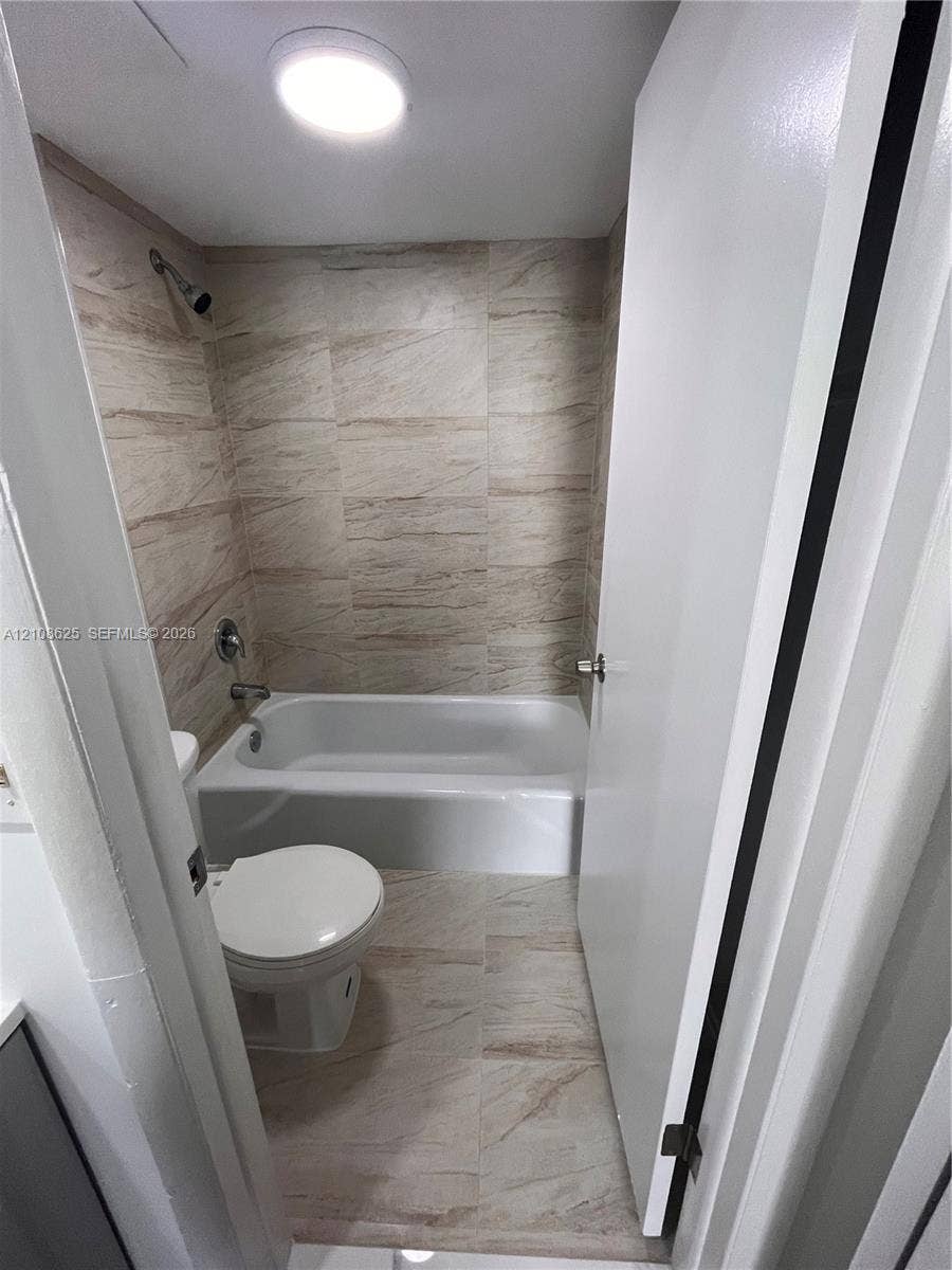 3650 Inverrary Drive, #1Q, Lauderhill, FL 33319 Bathroom featuring a full-size bathtub with a showerhead, wall-to-wall neutral tile surround, matching floor tiling, and a flush-mount ceiling light fixture