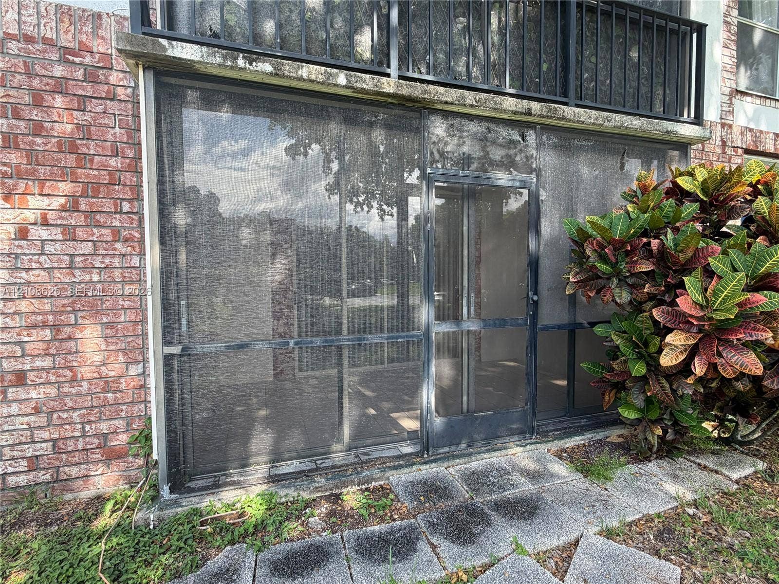3650 Inverrary Drive, #1Q, Lauderhill, FL 33319 Screened-in enclosure featuring a red brick exterior, stone paver pathway, and black metal balcony railing
