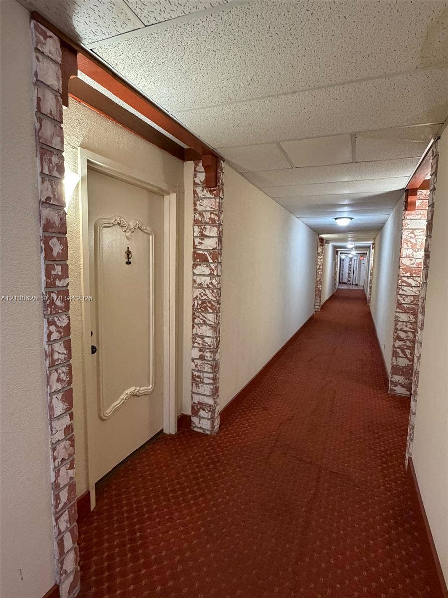 3650 Inverrary Drive, #1Q, Lauderhill, FL 33319 Hallway featuring decorative brick-clad columns, wood-beam accents, and recessed lighting