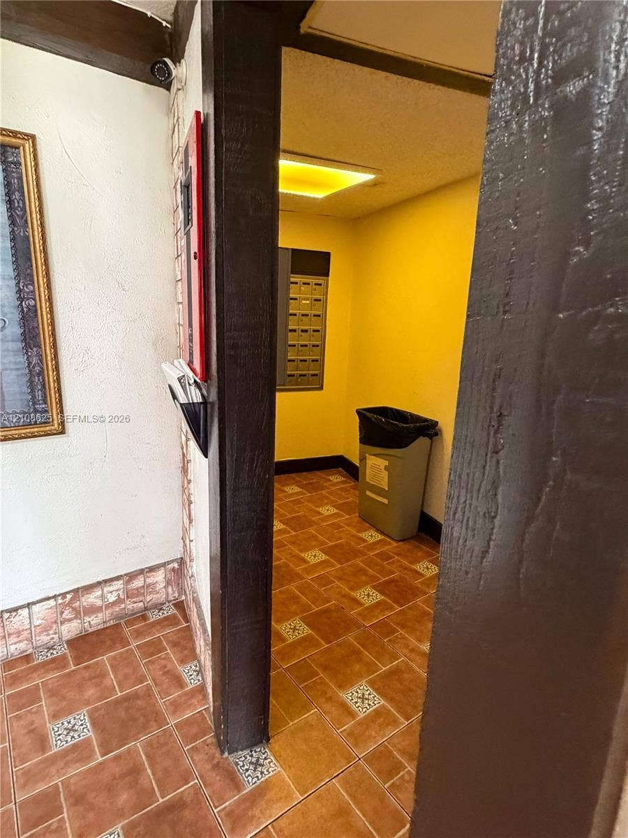 3650 Inverrary Drive, #1Q, Lauderhill, FL 33319 Textured wall surfaces, dark wood-finish structural trim, square ceramic tile flooring with decorative inlay accents, and built-in metal mailboxes