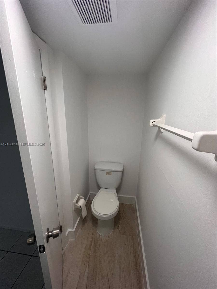 3650 Inverrary Drive, #1Q, Lauderhill, FL 33319 White porcelain commode, wood-finish flooring, and wall-mounted towel bar