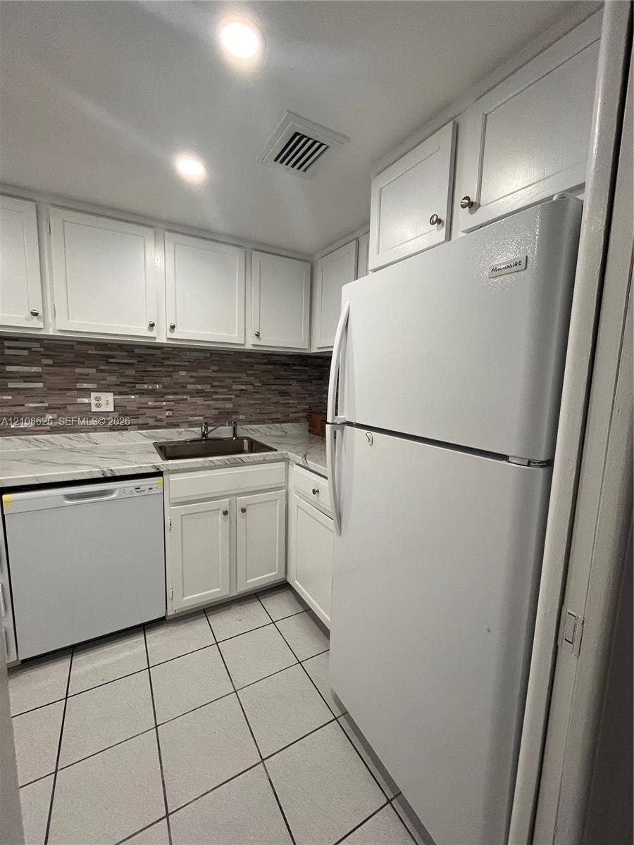 3650 Inverrary Drive, #1Q, Lauderhill, FL 33319 Kitchen featuring white cabinetry, stone-patterned countertops, a decorative mosaic tile backsplash, a stainless steel sink with a high-arch faucet, and square ceramic tile flooring