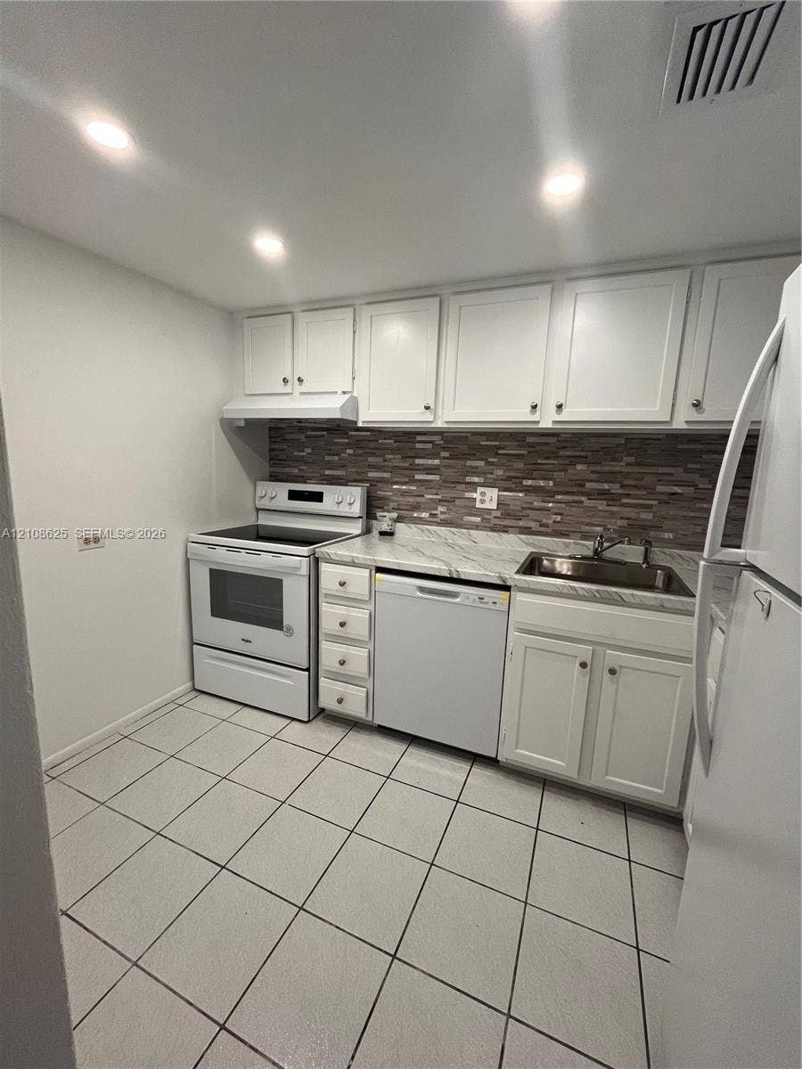 3650 Inverrary Drive, #1Q, Lauderhill, FL 33319 Kitchen featuring white cabinetry, stone-patterned countertops, a multi-tone tile backsplash, built-in appliances, and tile flooring