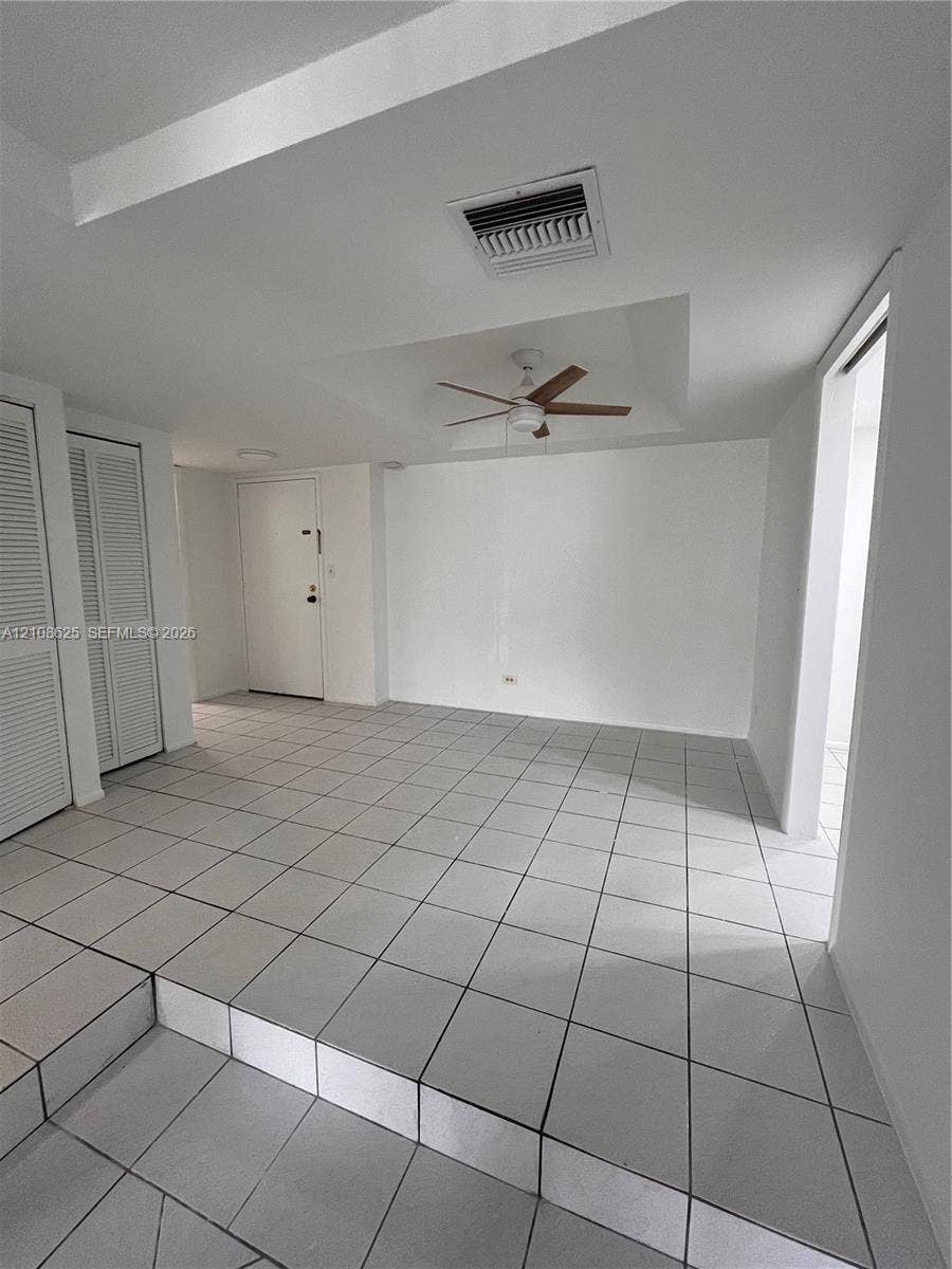 3650 Inverrary Drive, #1Q, Lauderhill, FL 33319 Interior space featuring large-format ceramic tile flooring, a tray ceiling, a ceiling fan, and dual louvered closet doors
