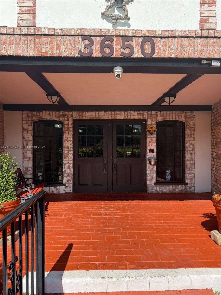 3650 Inverrary Drive, #1Q, Lauderhill, FL 33319 Covered entryway featuring a painted brick porch, double wood-panel doors with glass panes, arched windows, and an exposed beam ceiling