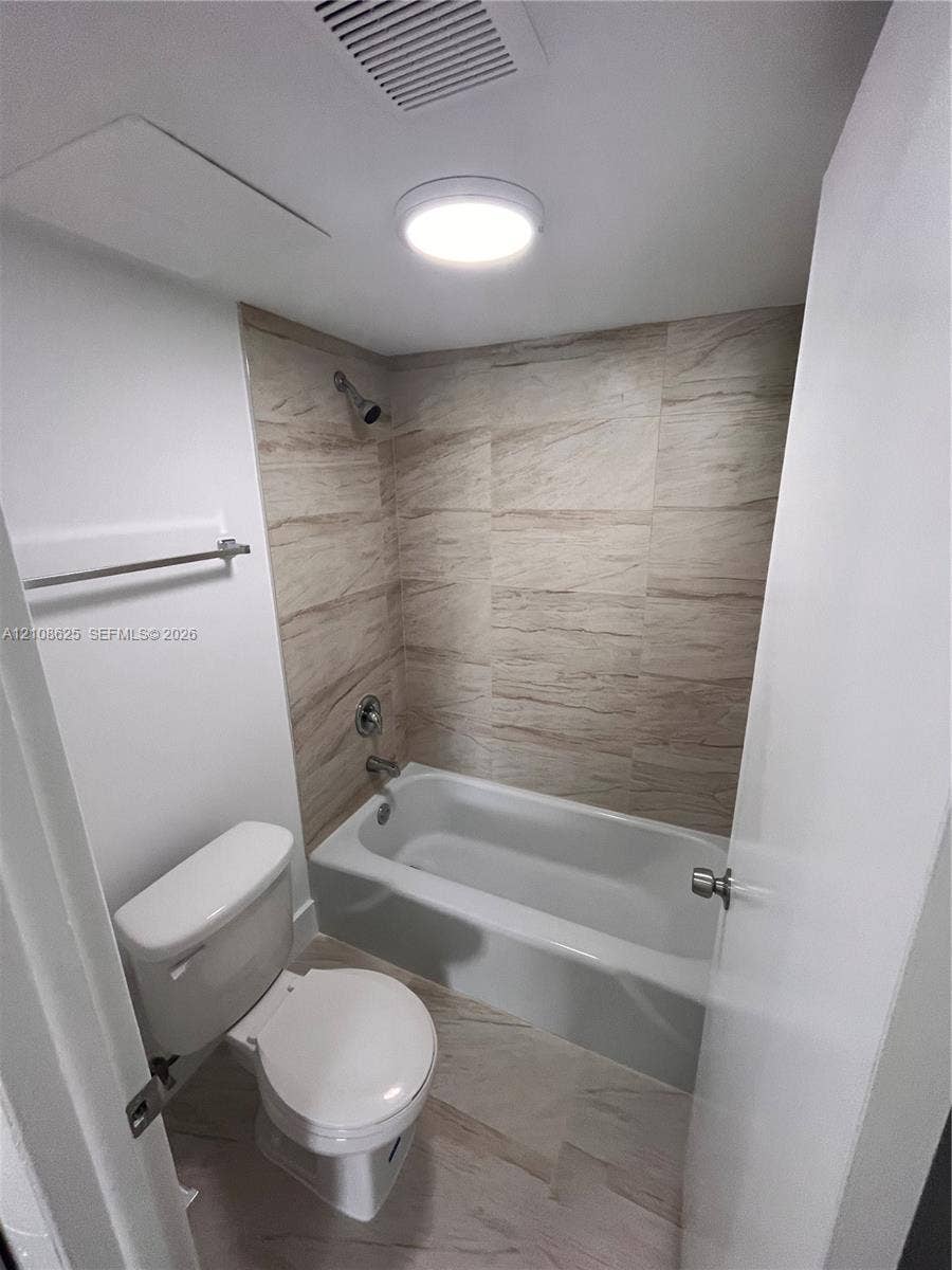 3650 Inverrary Drive, #1Q, Lauderhill, FL 33319 Bathroom featuring a tub with a neutral-toned tile surround, flush-mount lighting, and wall-mounted towel bar
