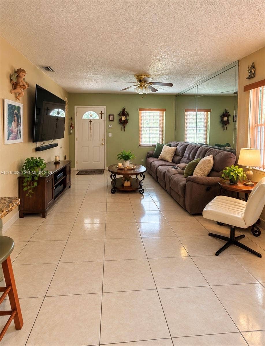 971 NE 156th Terrace, North Miami Beach, FL 33162 Ceramic tile flooring, mirrored wall accent, ceiling fan, and multiple windows with wood-finish blinds